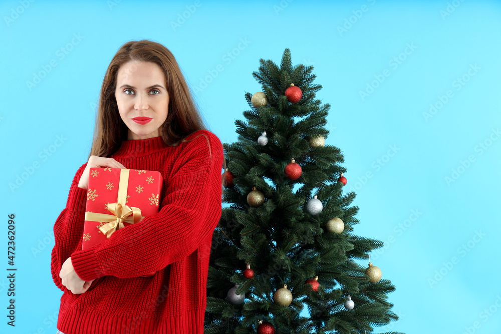 Attractive woman holds gift box on blue background with Christmas tree Attractive woman holds gift box on blue background with Christmas tree