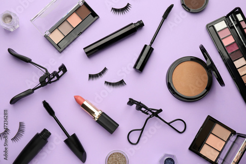 Eyelash curlers and makeup products on violet background, flat lay