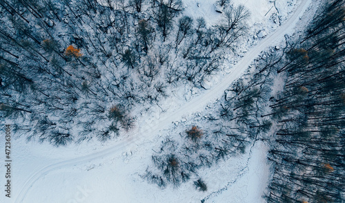 Aerial high angle view of snow covered mountain path and winter woodland. Country road track, bird's eye view. © Iryna