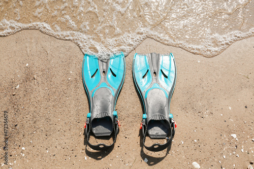 Pair of turquoise flippers on sand near sea, top view