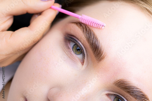 macro photography of the model's hairs the master combs the eyebrow hairs with a pink brush after the procedure long-term styling and lamination photo