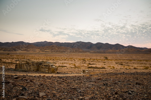 Wooden barn in the desert. Blue hour after sunset behind the mountains in the desert, Egypt Sandy land in the foreground, rocky mountains in the background. Little clouds on the sky during the sunset.
