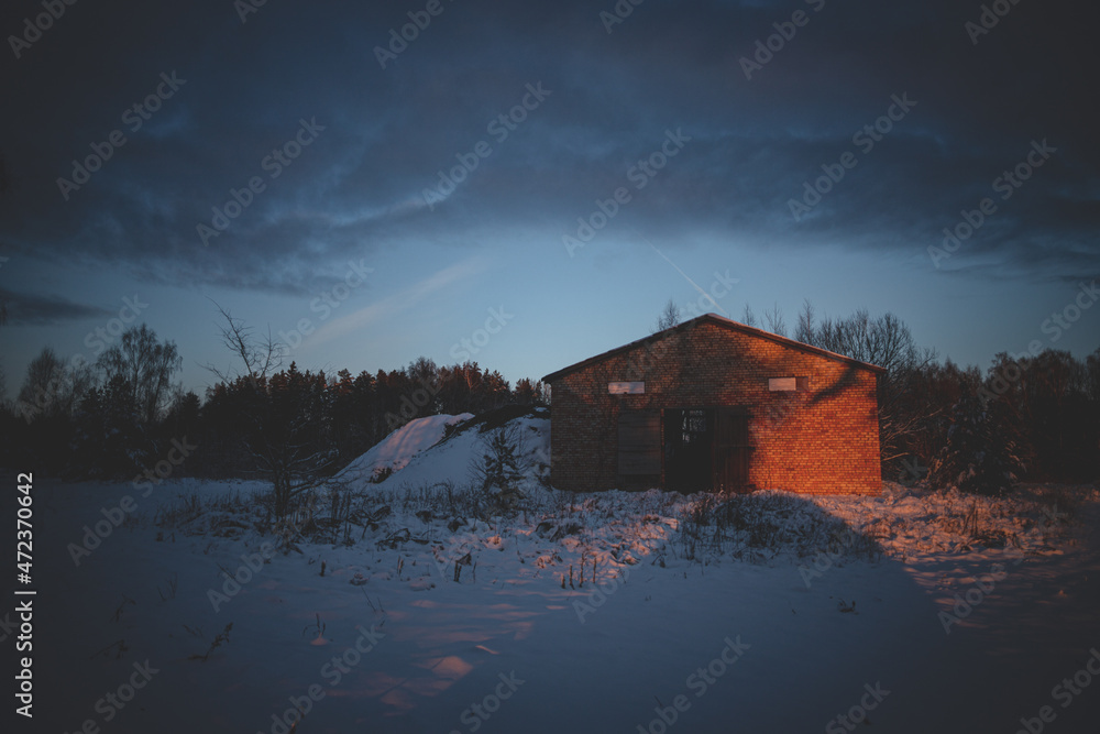 evening sunset sun ray shines on abandoned industrial agricultural orange brick building, snow on ground, cloudy beautiful sky