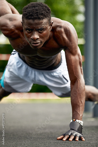 Muscular african man doing push ups in the park. Strong male athlete working out outdoors. © Georgii