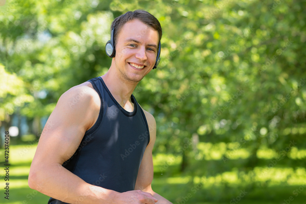happy young man doing workout outdoor. muscular smiling guy running in the park, training, listening music in headphones. sport, fitness healthy lifestyle concept. happy young man doing workout outdoor. muscular smiling guy running in the park, training, listening music in headphones. sport, fitness healthy lifestyle concept.