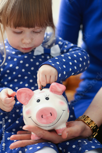 Cute little child putting coin cash into piggy bank container photo