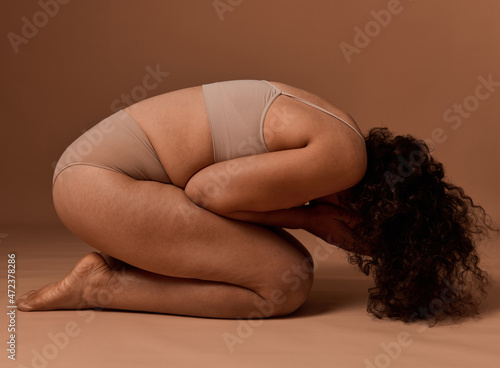Depressed woman in underwear with cellulite and stretch marks covers her face, doesn't accept herself and body because of framework established by society. Self-acceptance and body positivity concept
