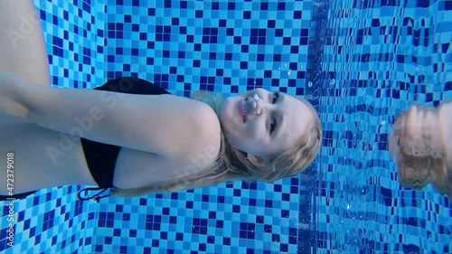 Fitted pretty woman in swimsuit,  diving under water in swimming pool. Caucasian girl vertical video underwater, relaxing on summer vacation..