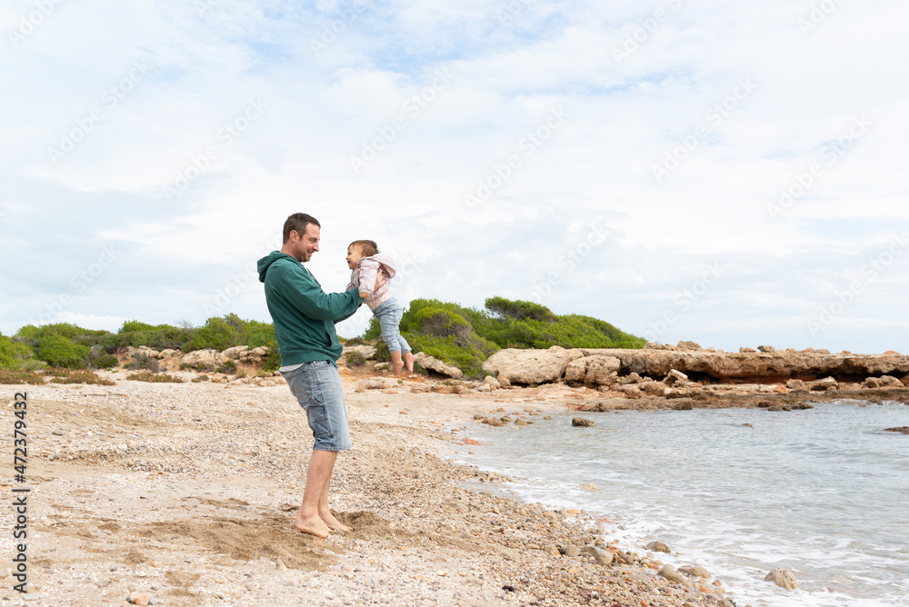 Father playing with his toddler girl at a mediterranean beach. Father and daughter having fun together. 
