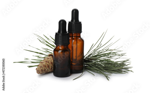 Glass bottles of essential oil and pine branch with cone on white background