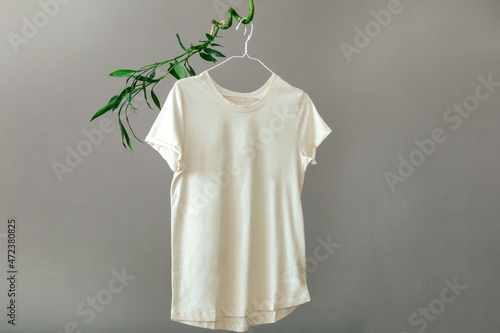 Beige T shirt hanging on hanger on plant Bamboo branches Isolated on gray background. Minimalistic Eco Concept Basic clothing T-shirt mockup. photo