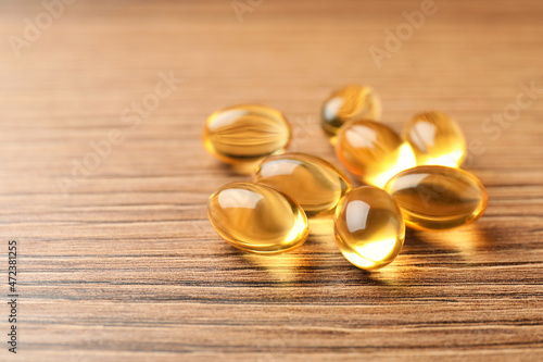 Dietary supplement capsules on wooden table, closeup. Space for text