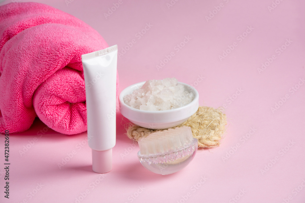 White cosmetic bottle, towels, massage brush, salt on pink background. Skin care, body treatment concept. Banner. Top view.