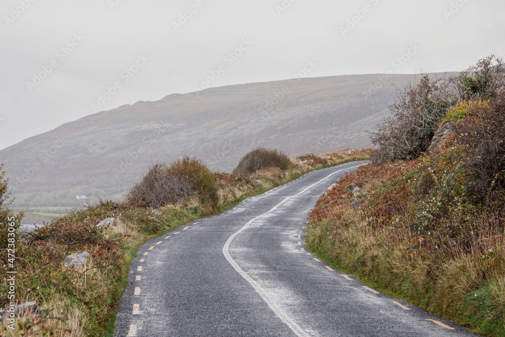 Small asphalt road by ocean. Burren area, Nobody. West of Ireland. Low cloudy sky. Transportation and tourism