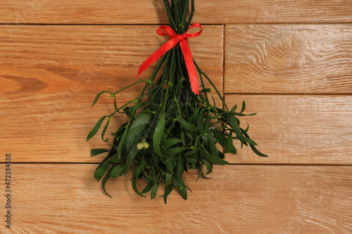 Mistletoe bunch with red bow on wooden table  top view. Traditional Christmas decor