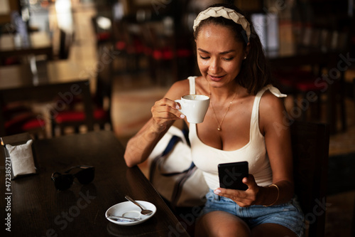 Stylish young woman drinking coffee at cafe. Beautiful girl enjoy in fresh coffee