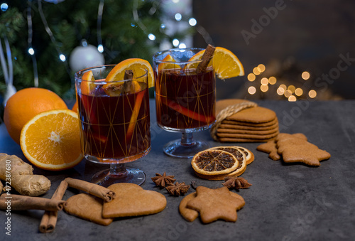 mulled wine on a dark table with gingerbread cookies, oranges, cinnamon on the background of a Christmas tree