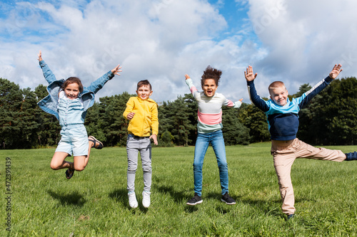 childhood  leisure and people concept - group of happy kids jumping and having fun at park