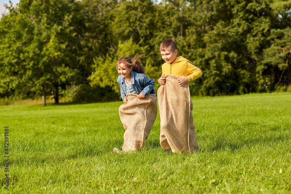 Obraz premium childhood, leisure and people concept - two happy children playing bag jumping game at park