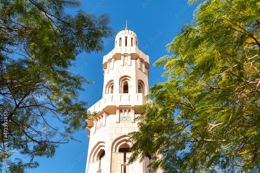 The tamarind tree grows in front of the minaret Tower, behind the branches of the tree there is a beautiful view of the mosque tower, a view of the mosque and a green tree in summer