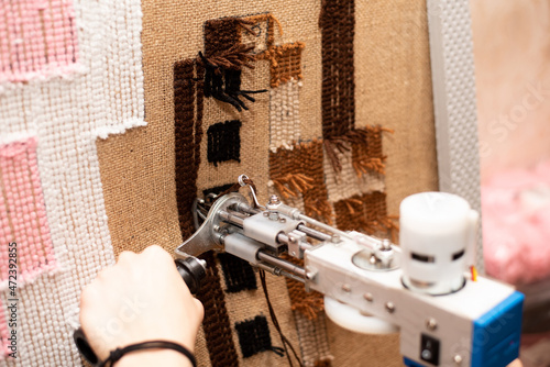 The process of making a tufting rug. Tufting a pistol in female hands against the background of a handmade brown tank rug on sacking.