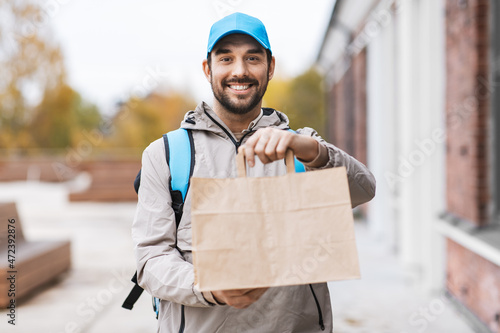 food shipping, profession and people concept - happy smiling delivery man with thermal insulated bag and order in city