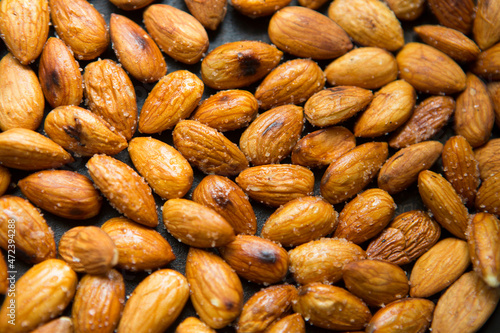 Filled frame background wallpaper shot of a bunch of crunchy roasted almonds with sea salt on a black background