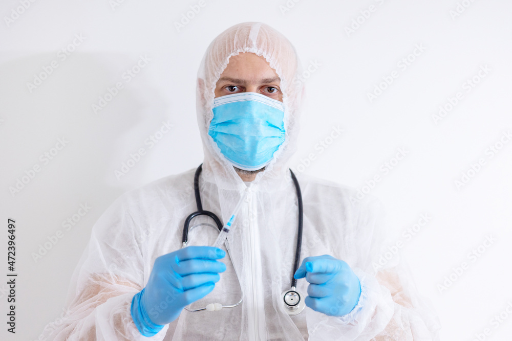 young male doctor in protective suit and blue protective gloves and mask with stethoscope and syringe, invitation to vaccination young male doctor in protective suit and blue protective gloves and mask with stethoscope and syringe, invitation to vaccination