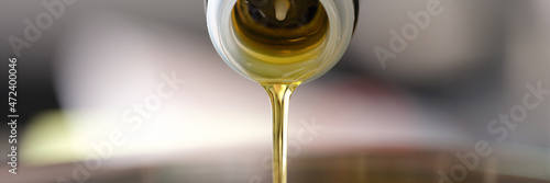 Clear olive oil is poured from dispenser bottle into saucepan closeup