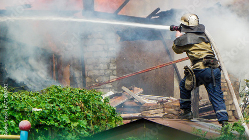 Kamianske, Ukraine - July 08, 2011: firefighter extinguishes a burning building with water, rescue man spraying water on a burning building