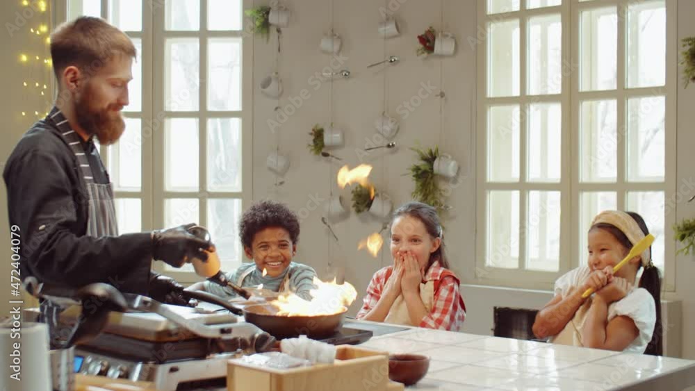 Excited multiethnic kids watching chef lighting and flambeing dish in pan during cooking masterclass Excited multiethnic kids watching chef lighting and flambeing dish in pan during cooking masterclass