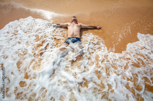 A handsome young man lying in the clear water at the beach seashore