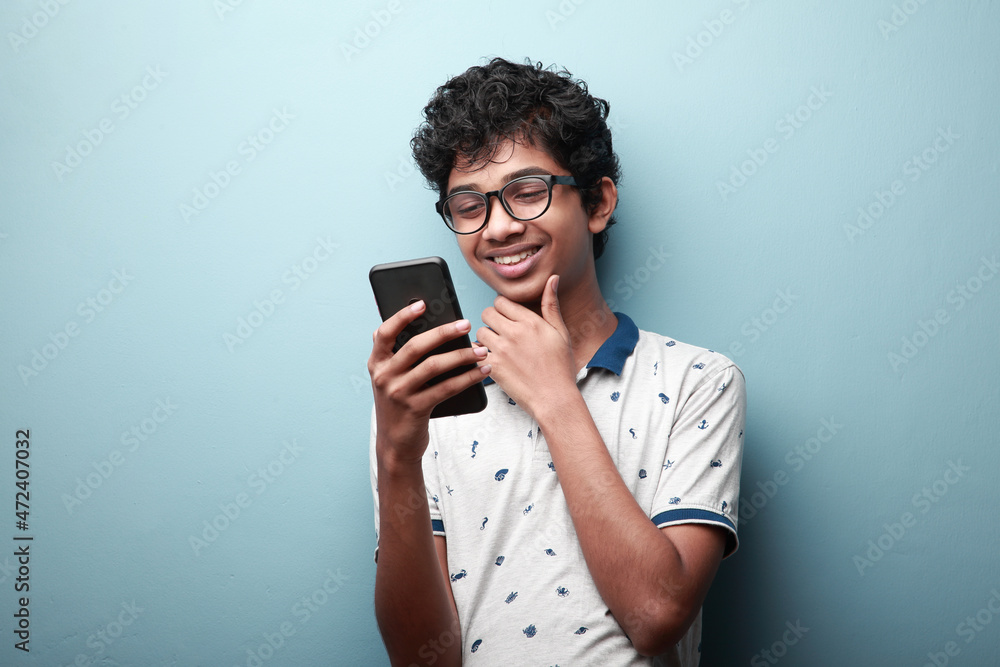 Young boy of Indian origin looking at his mobile phone with a smiling face expression Young boy of Indian origin looking at his mobile phone with a smiling face expression
