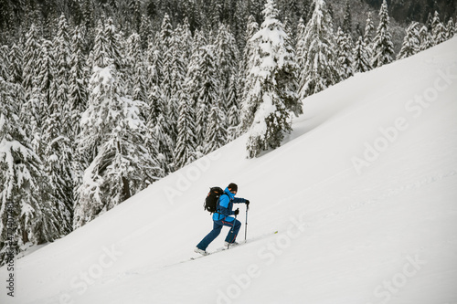 view of man with trekking poles climbing up snow-covered mountain against background of trees