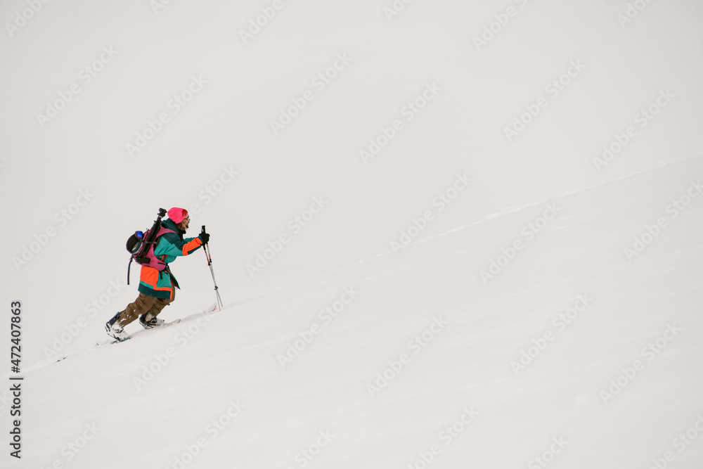 man skier in a bright colored ski suit climbs up a snowy mountain.