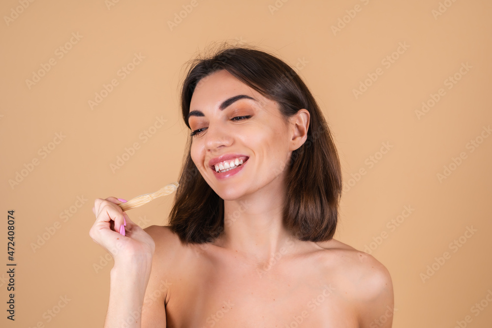 Young topless woman on beige background naked shoulders holds an ecological wooden toothbrush, taking care of the nature and a tooth Young topless woman on beige background naked shoulders holds an ecological wooden toothbrush, taking care of the nature and a tooth