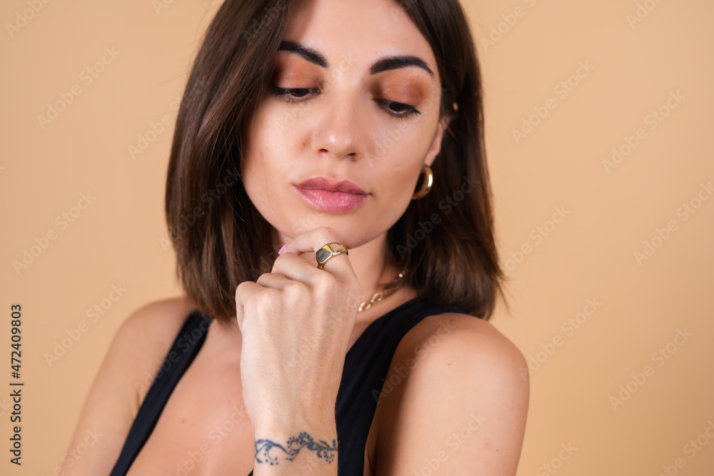 Close fashion portrait of young woman on beige background in black bodysuit with gold cuts, chain, ring posing Close fashion portrait of young woman on beige background in black bodysuit with gold cuts, chain, ring posing