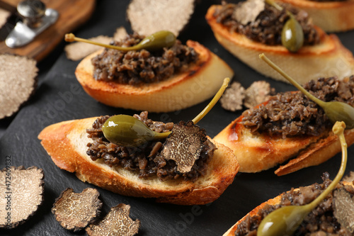 Tasty bruschettas with truffle paste and capers on black table, closeup
