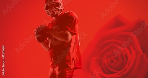 Confident young athlete holding american football's ball over red rose background