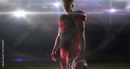 Portrait of confident player wearing jersey holding helmet at illuminated american football stadium