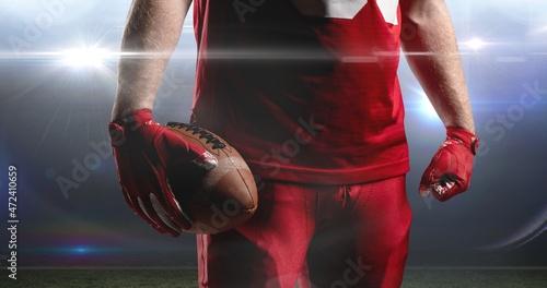 Midsection of american footballer holding wearing red jersey and gloves ball at stadium