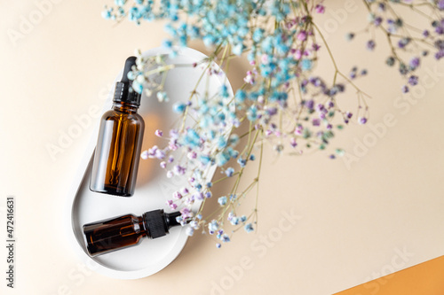 Amber glass bottles with aromatic oil or serum on a stone tray with gypsofila flowers above. Natural Organic Spa Cosmetic concept. Top view. photo