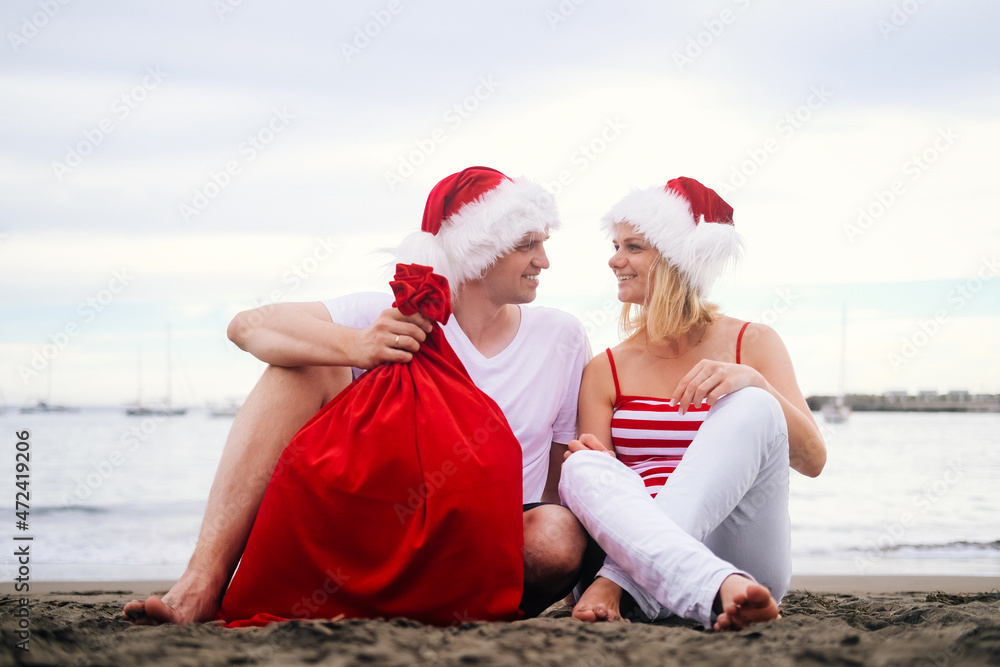 Obraz premium Happy family in Santa Claus hats celebrating Christmas on beach. Smiling people traveling to warm countries on winter tour. New Year and Christmas tourists
