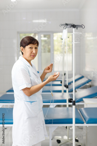 Vertical portrait of a senior female nurse in middle asia Kazakhstan clinic intravenous drip hospital room