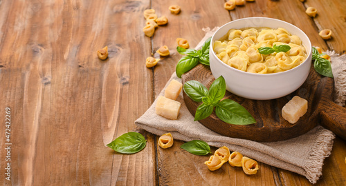 Tortellini soup, brodo on a wooden board with basil and parmesan. Cuisine from Bologna and Emilia Romagna: Cappelletti, fresh egg pasta with meat and vegetables filling. Copy space. Banner photo