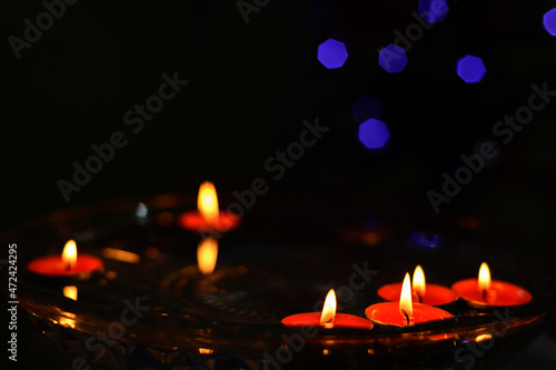 Floating candles on the water in the dark, orange cylindrical wax candles burning close up. © nilanka