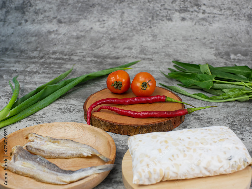 salted fish, raw tempeh and vegetables on a wooden cutting board salted fish, raw tempeh and vegetables on a wooden cutting board