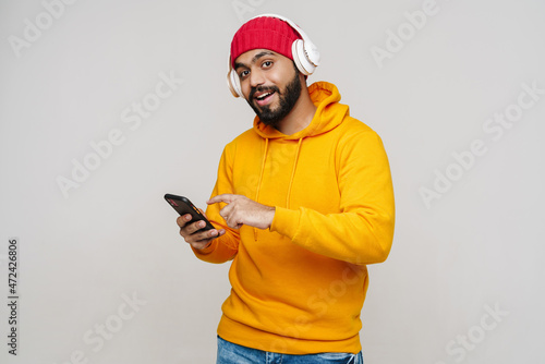 Bearded south asian man in headphones smiling and using cellphone