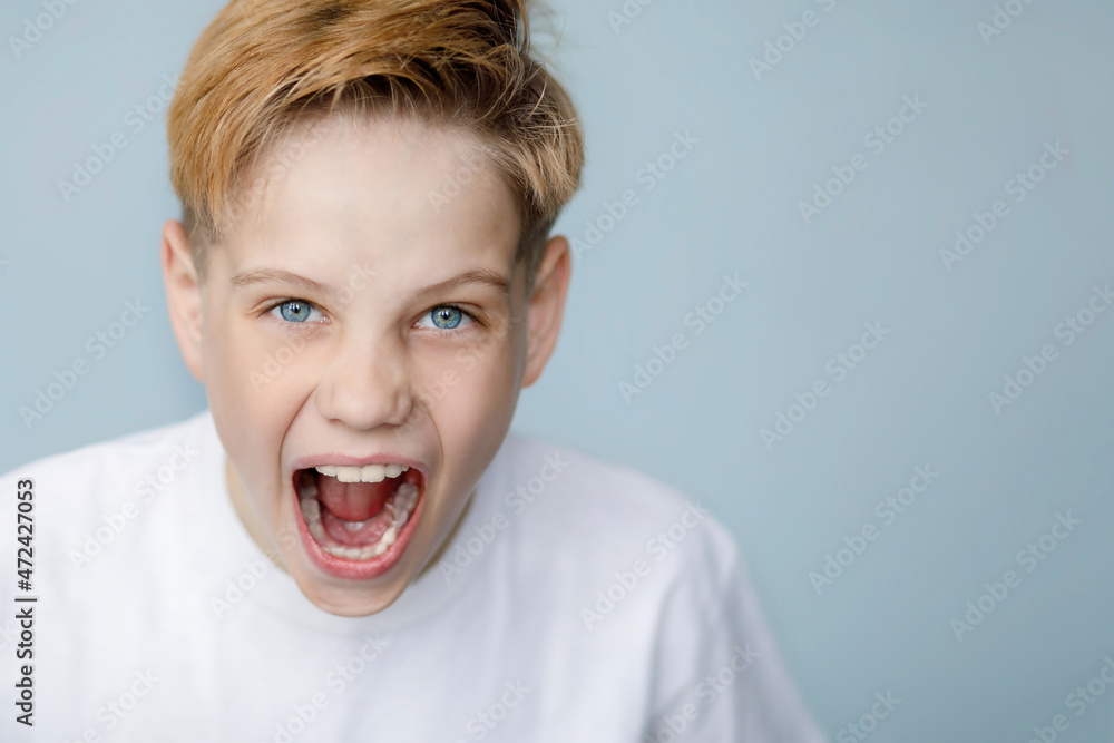 Teen boy screams strongly with wide open blue eyes, hopelessness, anger, emotions Teen boy screams strongly with wide open blue eyes, hopelessness, anger, emotions
