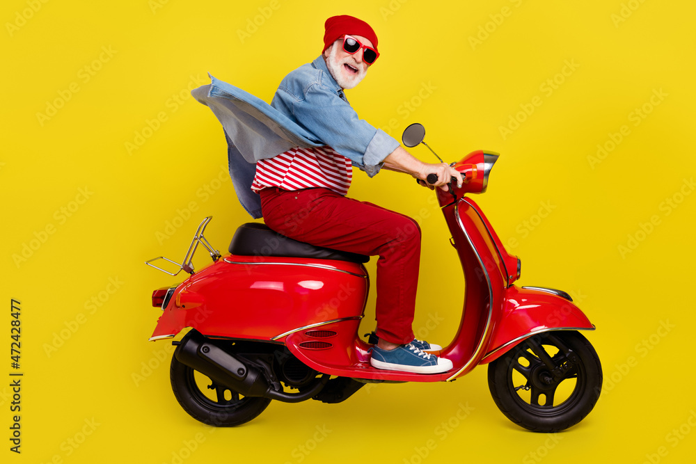Profile side view portrait of elderly retired pensioner cheery man riding moped isolated over bright yellow color background Profile side view portrait of elderly retired pensioner cheery man riding moped isolated over bright yellow color background
